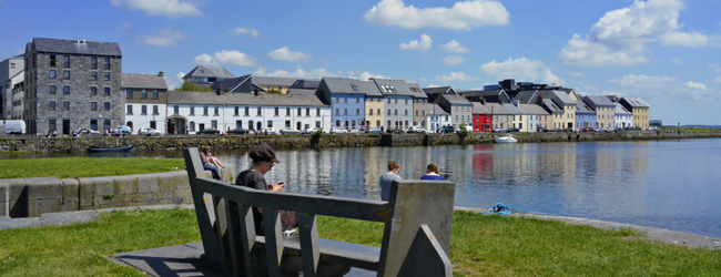 Promenade in Galway lädt zum Entspannen ein Menschen sitzen an der Promenade und entspannen im Sonnenschein vor den Häusern von Galway